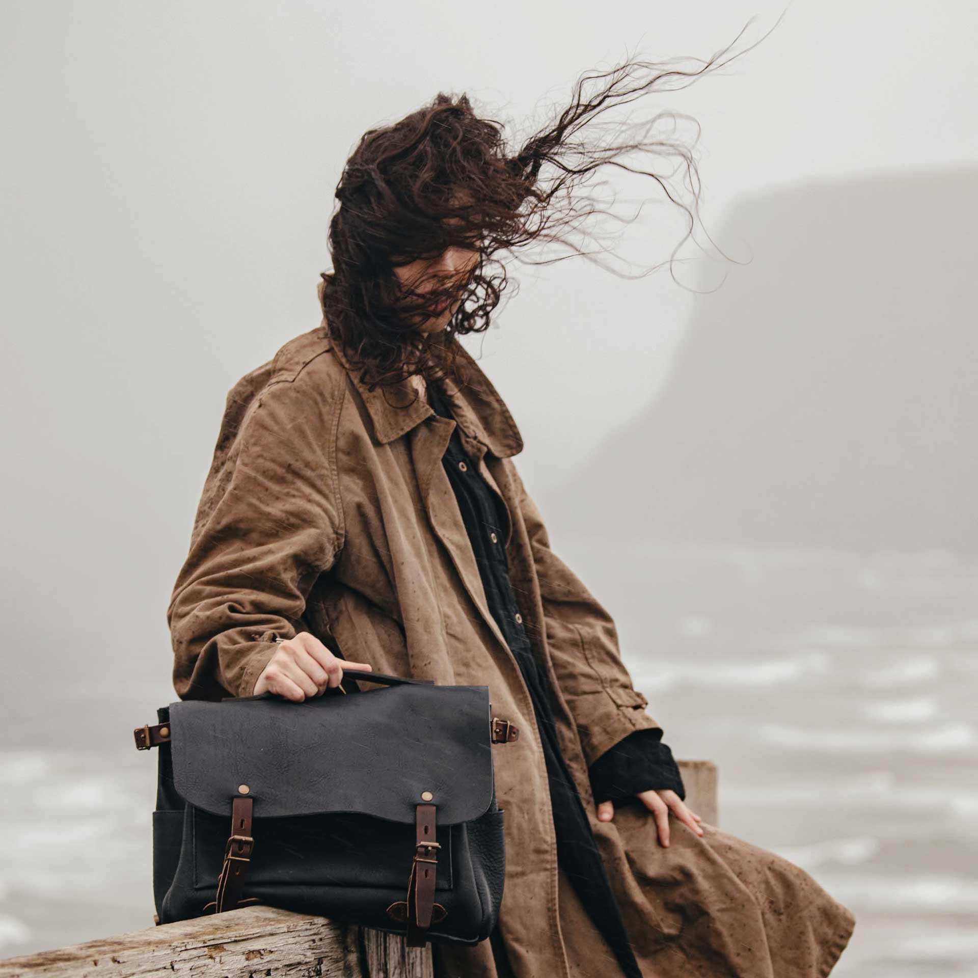 A women carry a leather messenger bag in front of him in a sea landscape.
