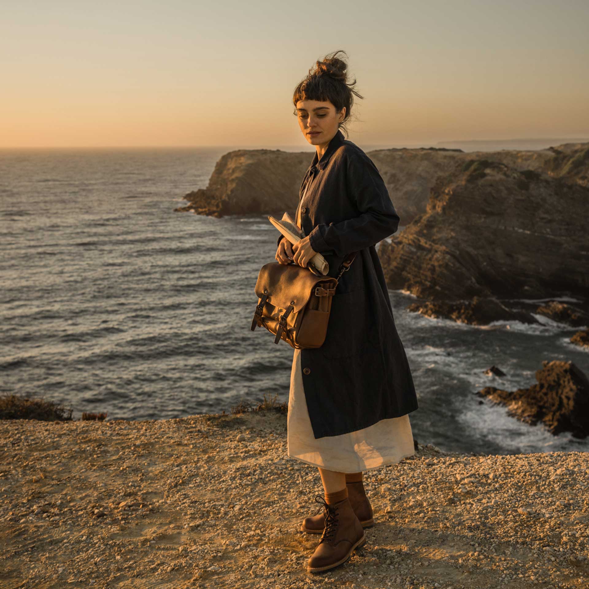 Une femme en bord de mer porte sa besace en cuir marron.