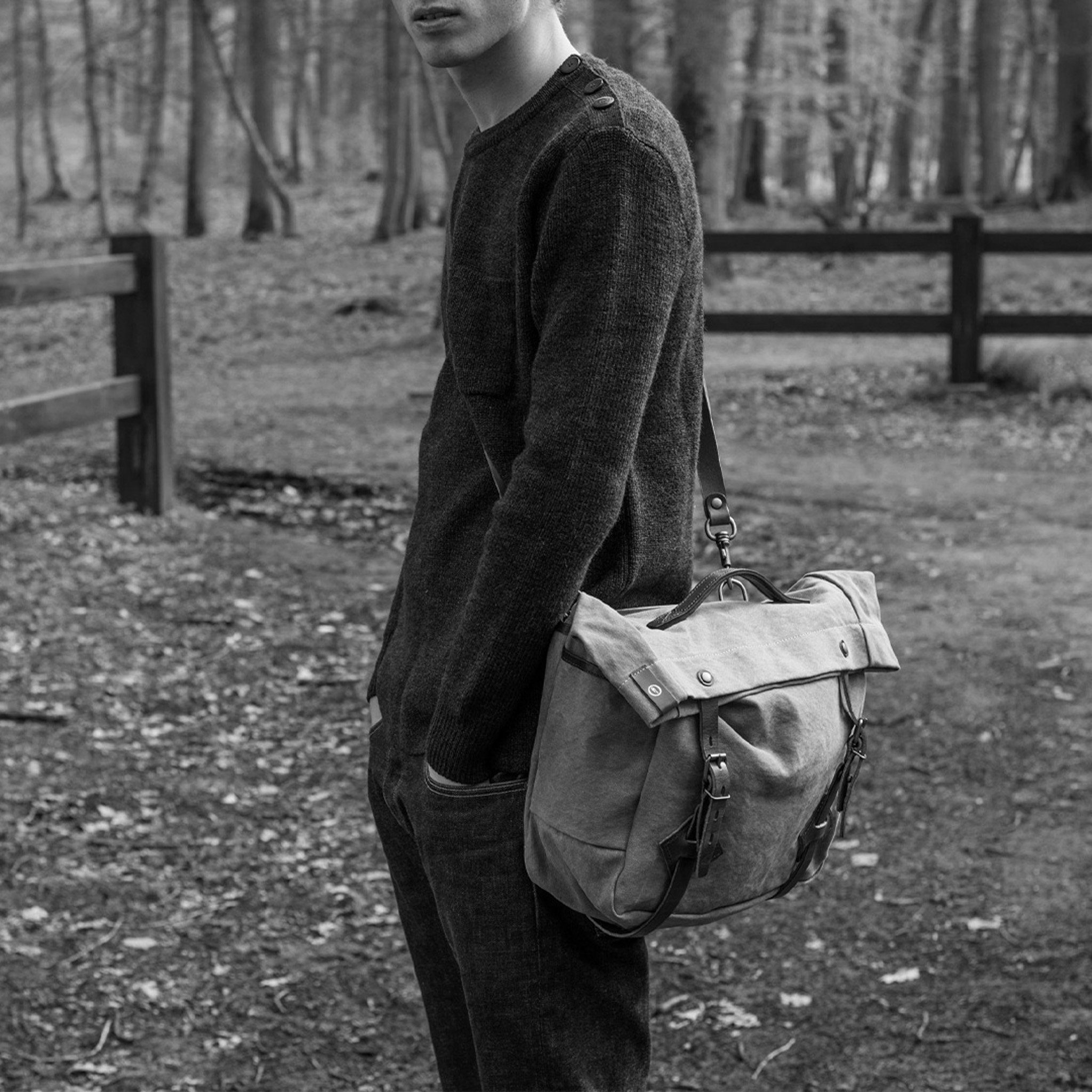 Black and white photo of a man in the forest, carrying a musette bag on his shoulder.