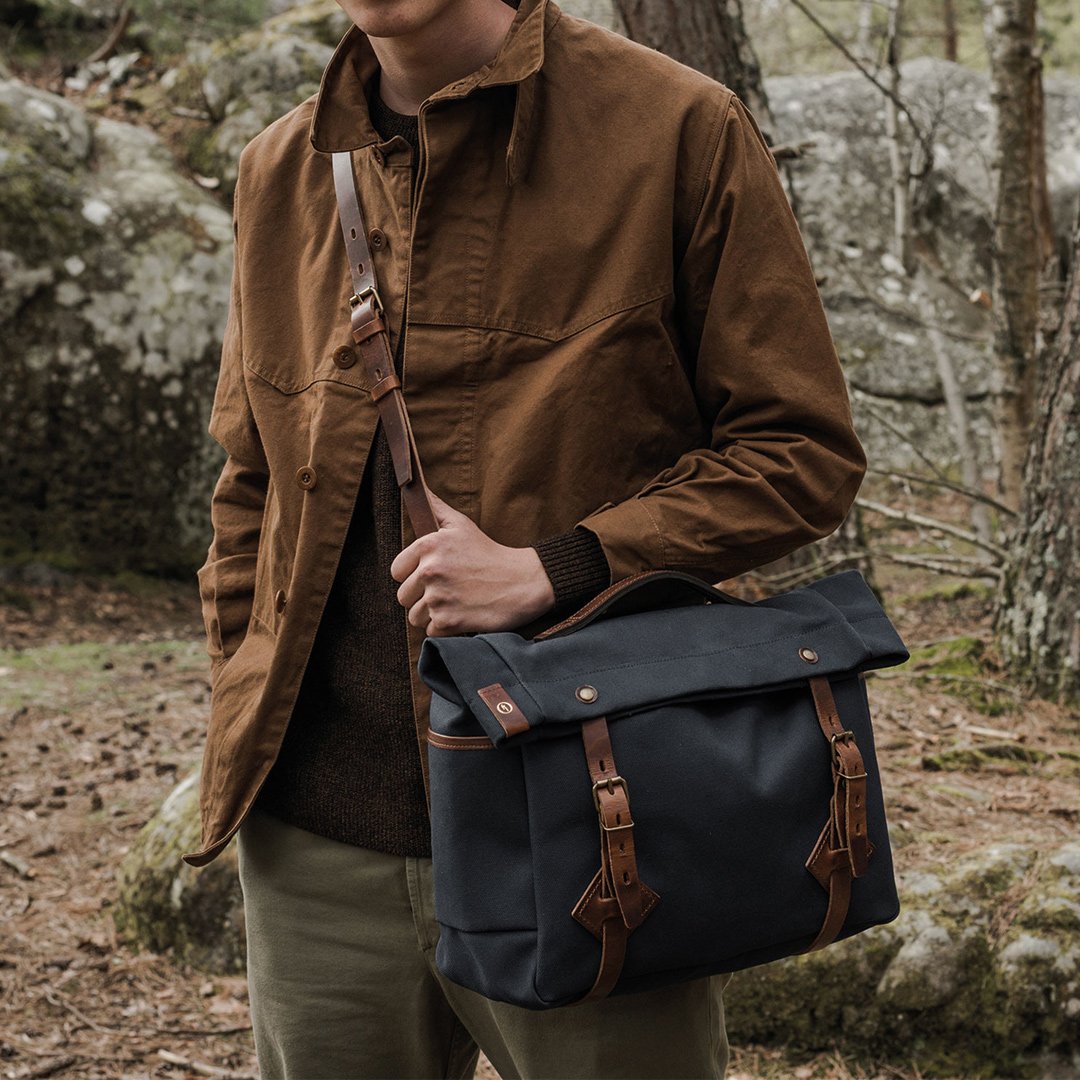 A man is carrying a Gaston bag in Navy Blue on his shoulder strap