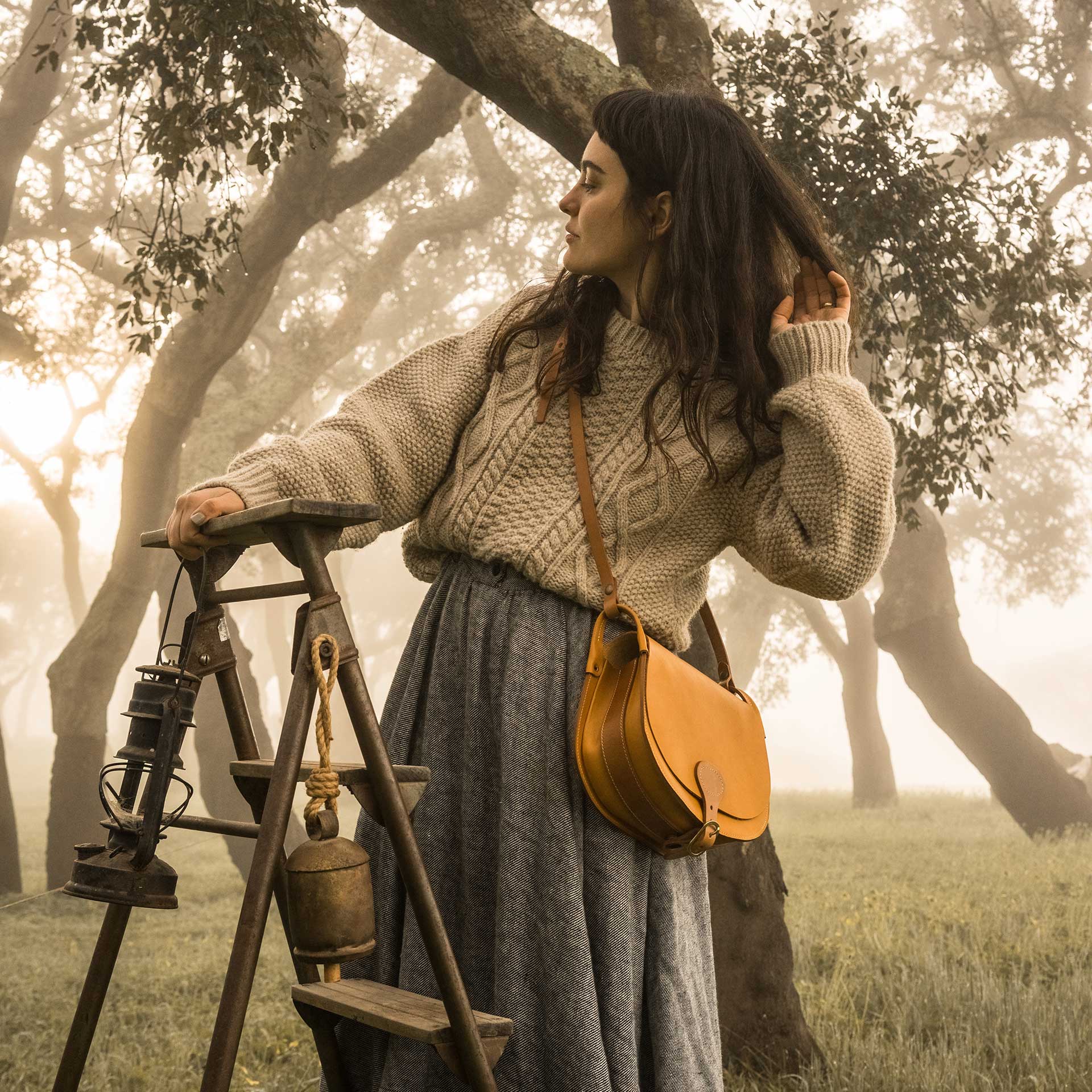 Une femme dans la foret pose sur un tabouret avec une gibeciere en bandouilière