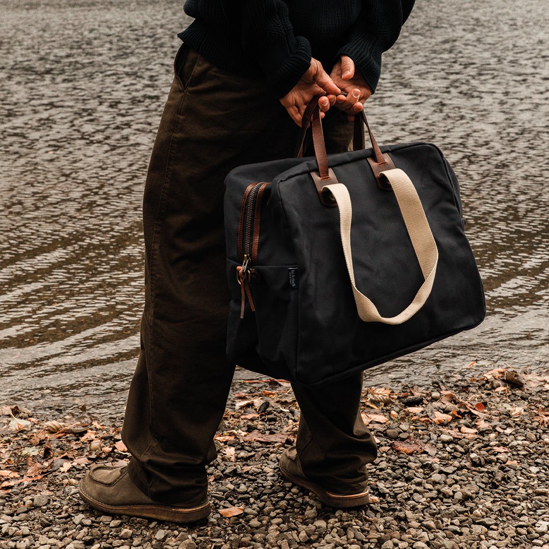 Un homme de dos devant un lac porte a la main le sac aviateur Missak