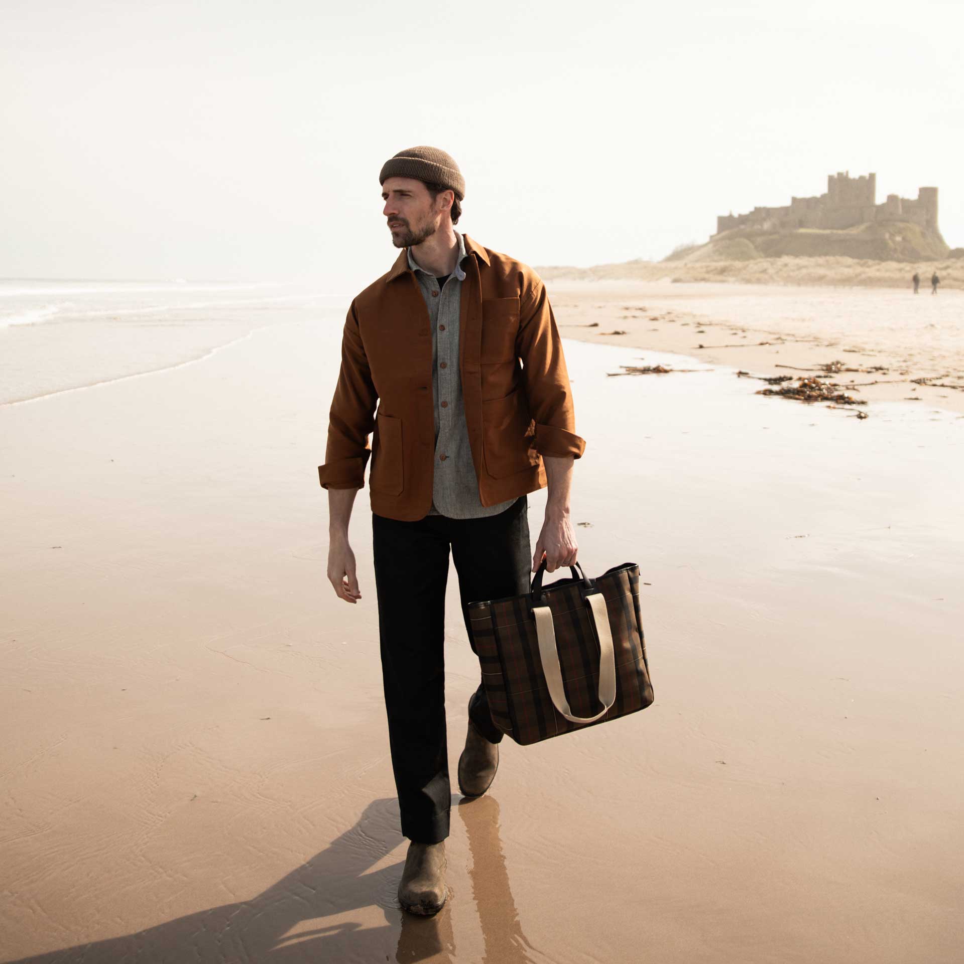 un homme marche sur la palge avec un sac cabas tartan