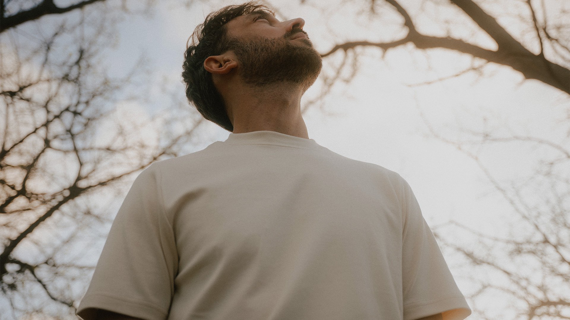 Un jeune homme en t-shirt regarde en l'air sous un arbre 