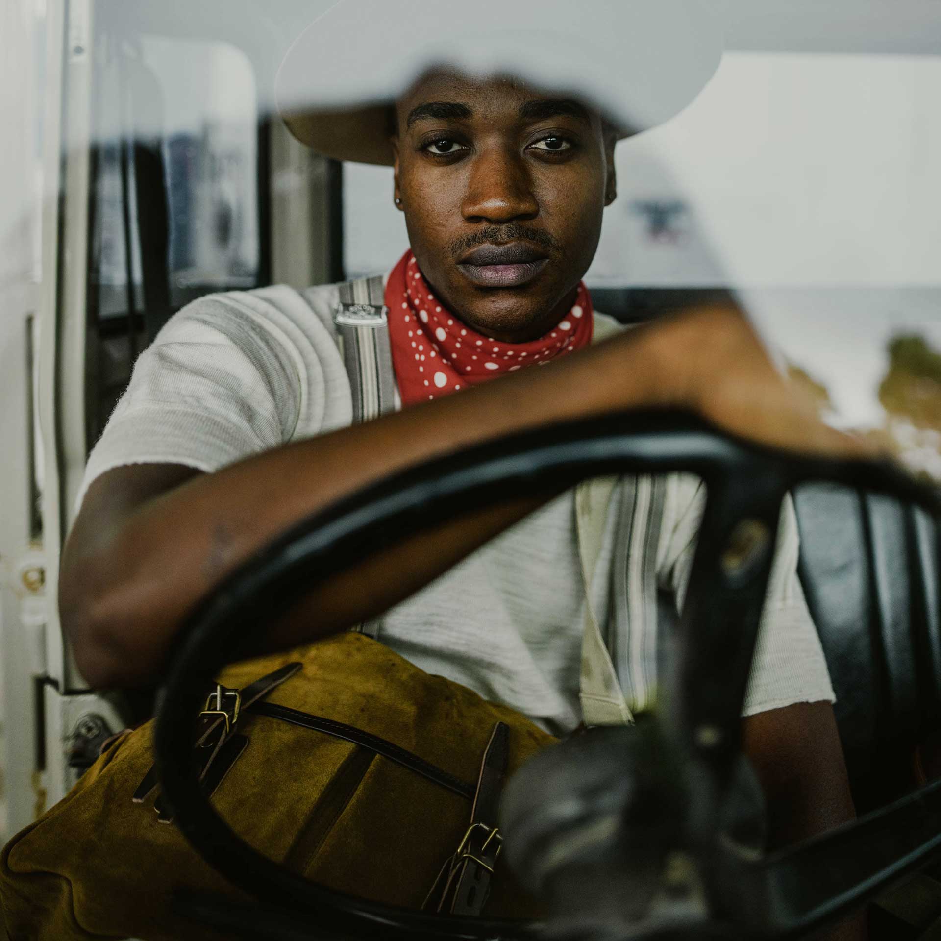 Un jeune homme au look aventurier porte une musette dans son 4x4