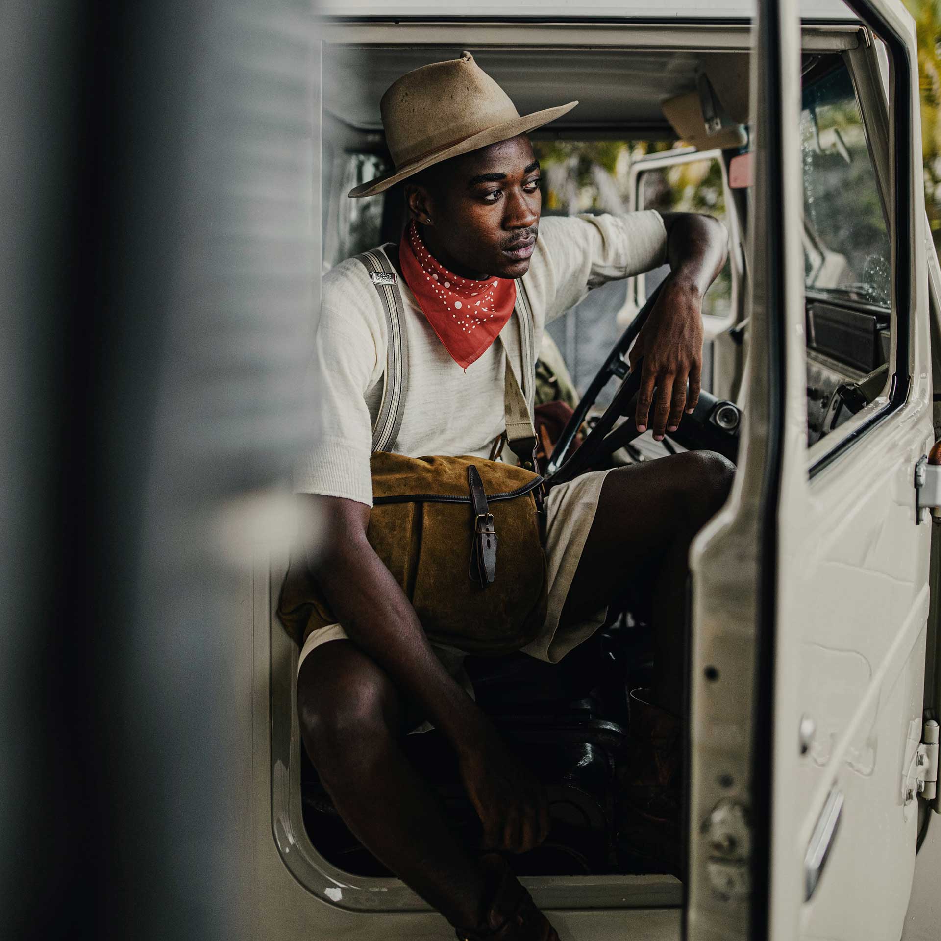 Un jeune homme au look aventurier porte une musette dans son 4x4