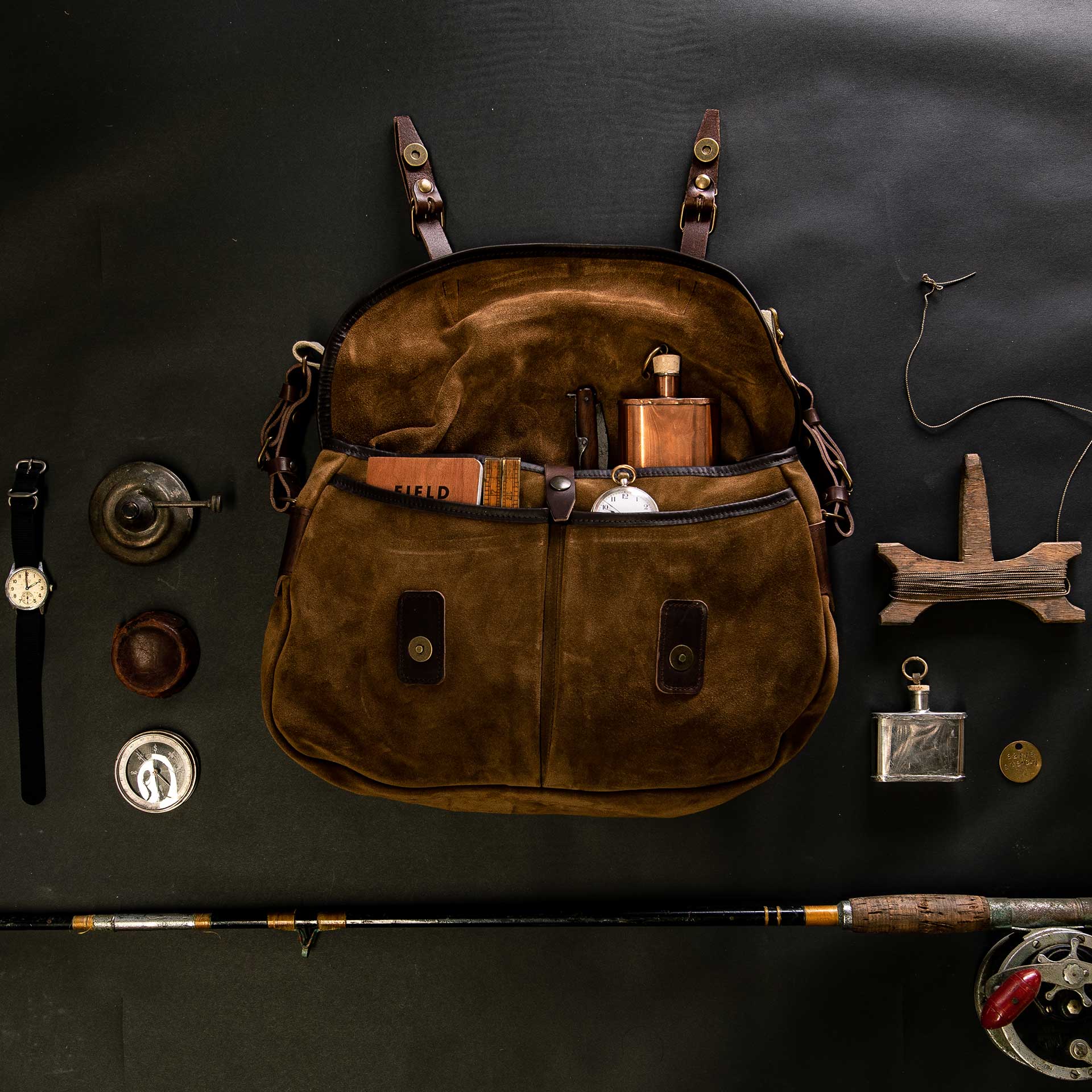 Musette du pecheur en cuir velours tabac posée sur un drap noir