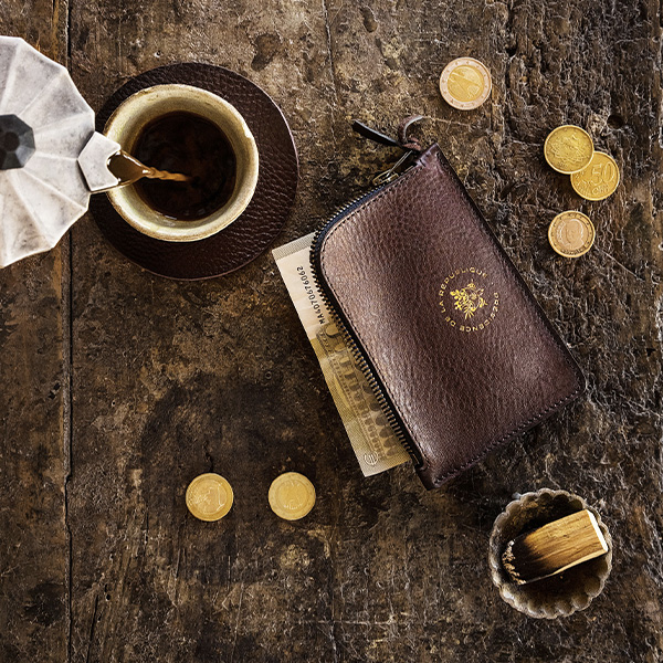 Porte monnaie en cuir sur une table en bois entouré de pièces 