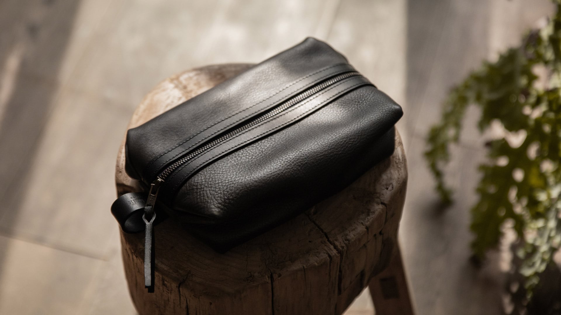 A man shaves in front of a mirror, and on the sink is a leather toiletry bag