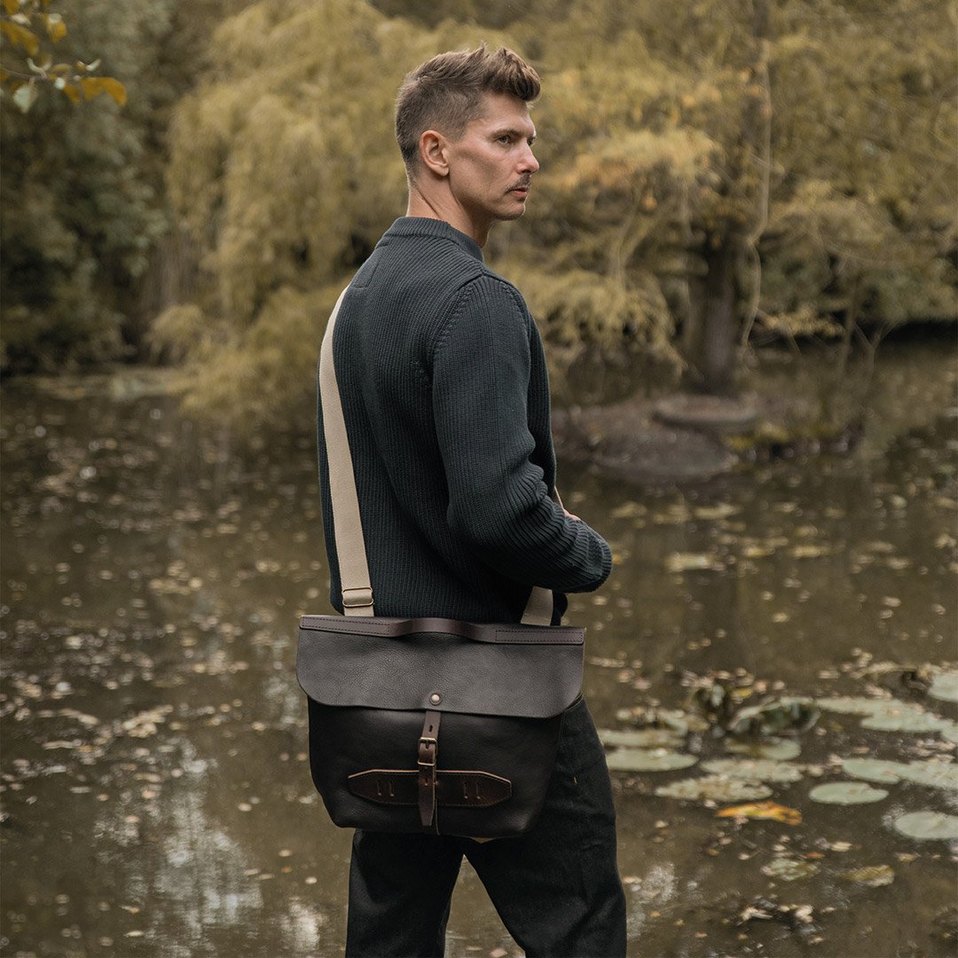 A man slings his elazar bag over his shoulder in front of a lake