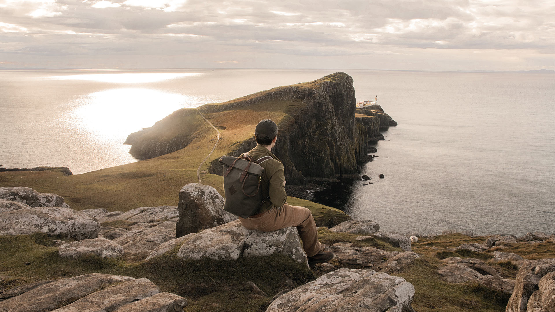 A man at the top of a cliff looks towards the horizon and carries the Woody canvas bag on his back.
