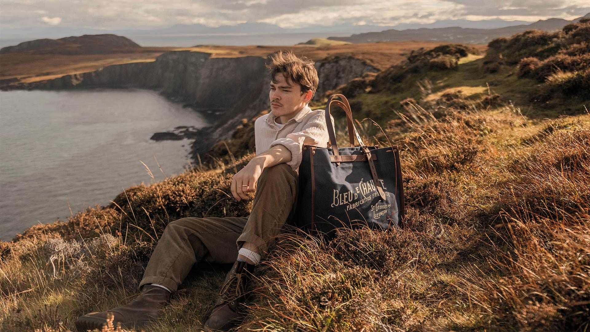 A man sits beside his shopping bag on the edge of a cliff