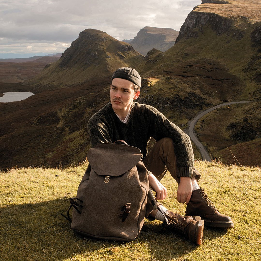 A man sitting in nature next to his leather backpack