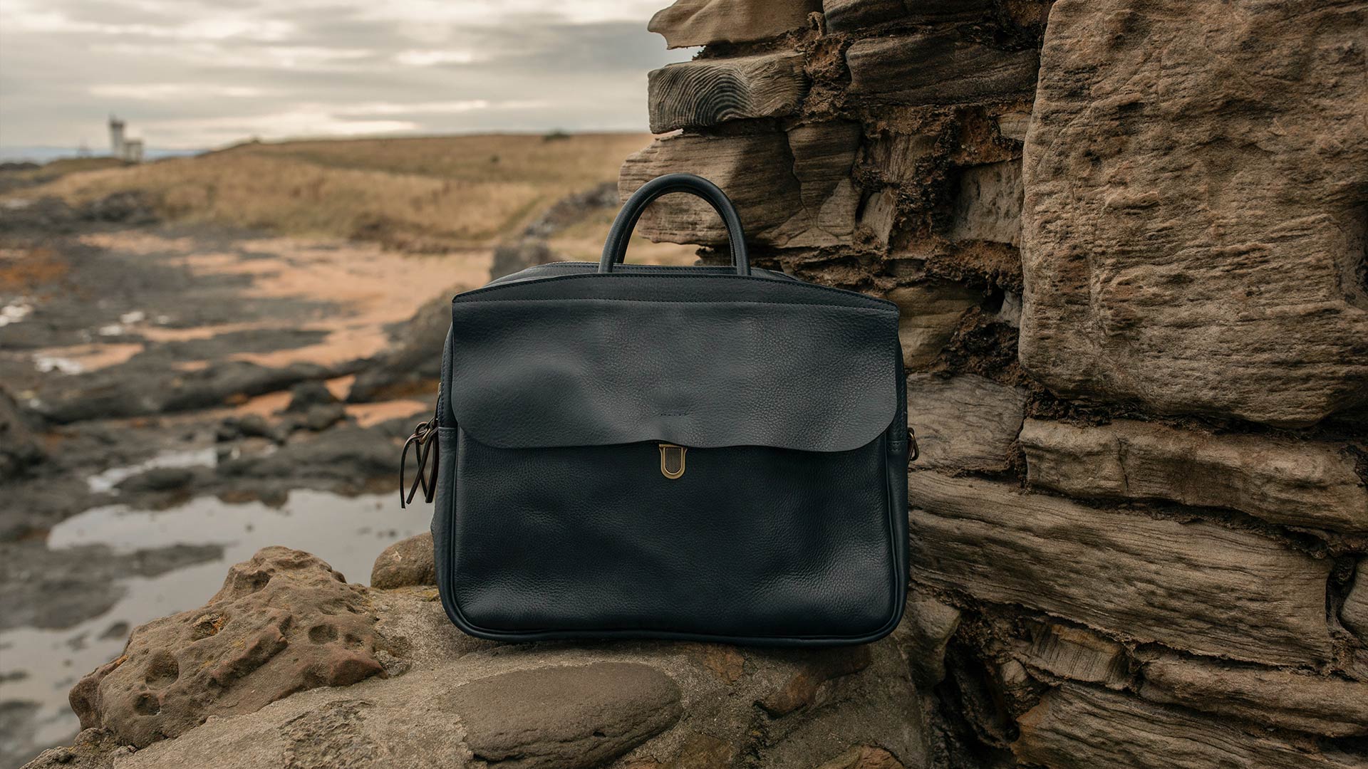 Sac en cuir bleu marine &agrave; rabat pos&eacute; sur des rochers en bord de mer