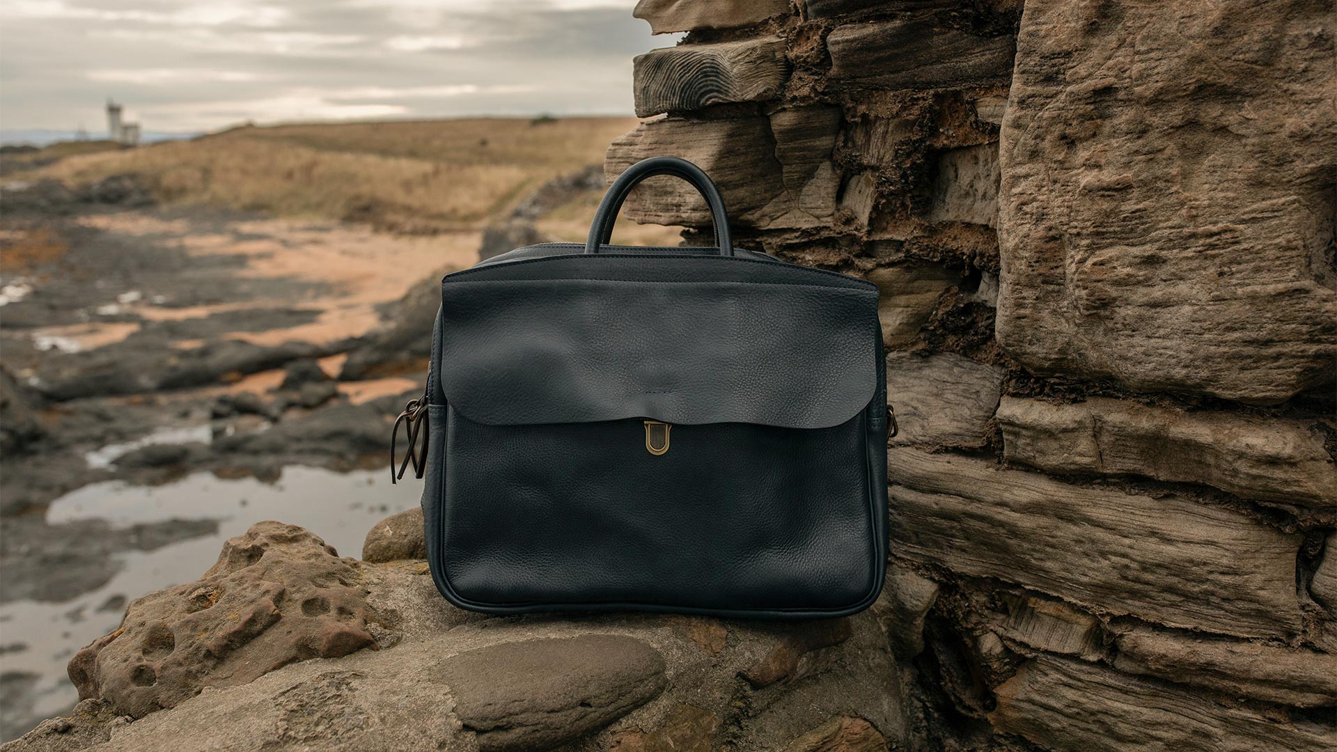 Zeppo leather computer bag on a low stone wall in a seaside landscape