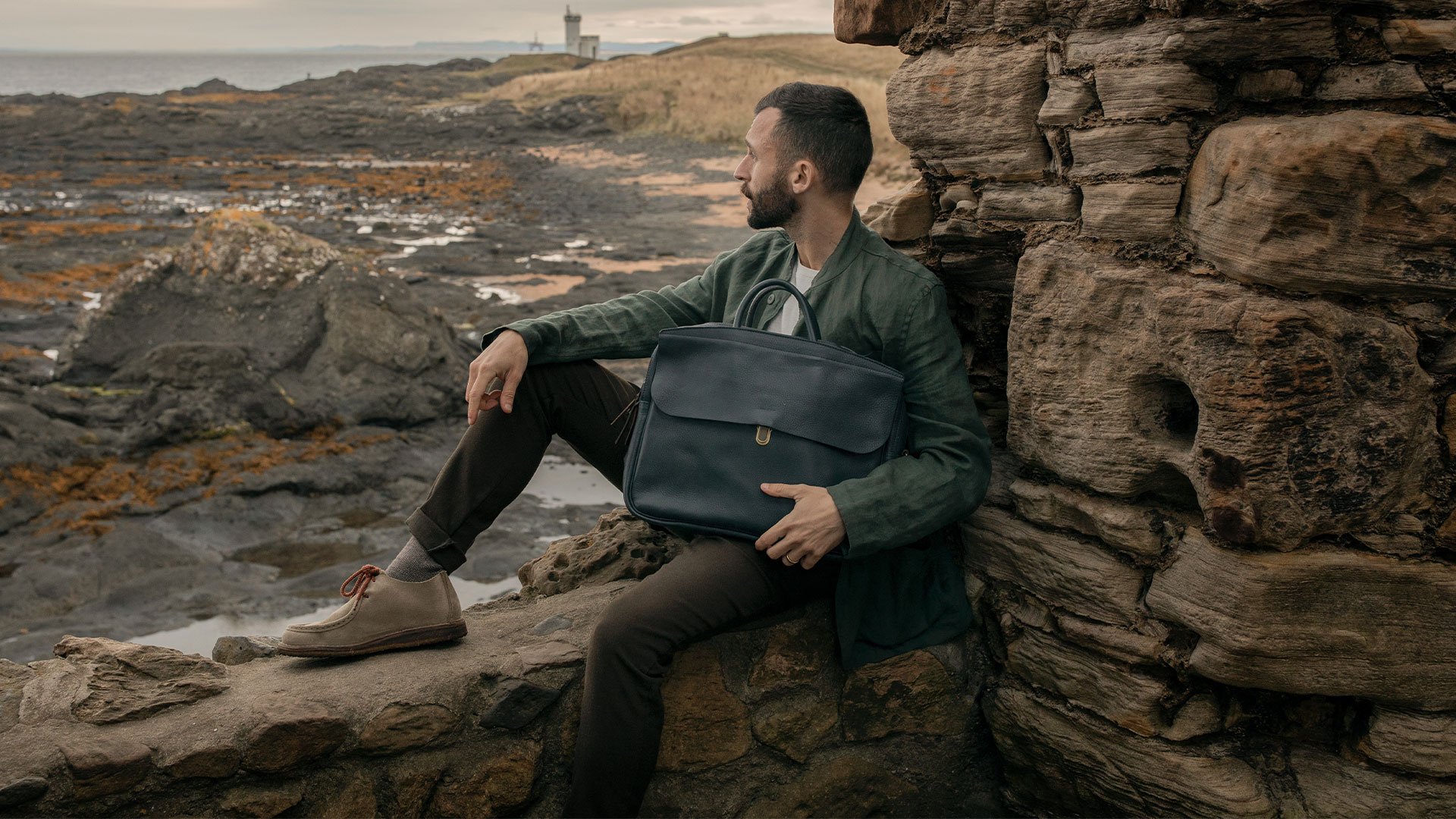 A young man carrying the Zeppo computer bag in a seaside landscape