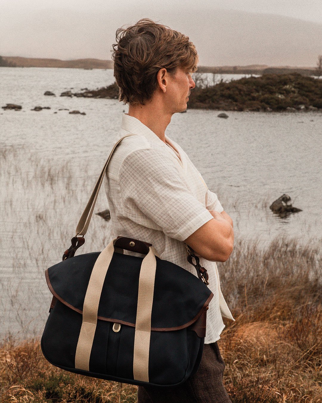 Un homme dans la nature porte à l'épaule la besace "musette business - navy" bm