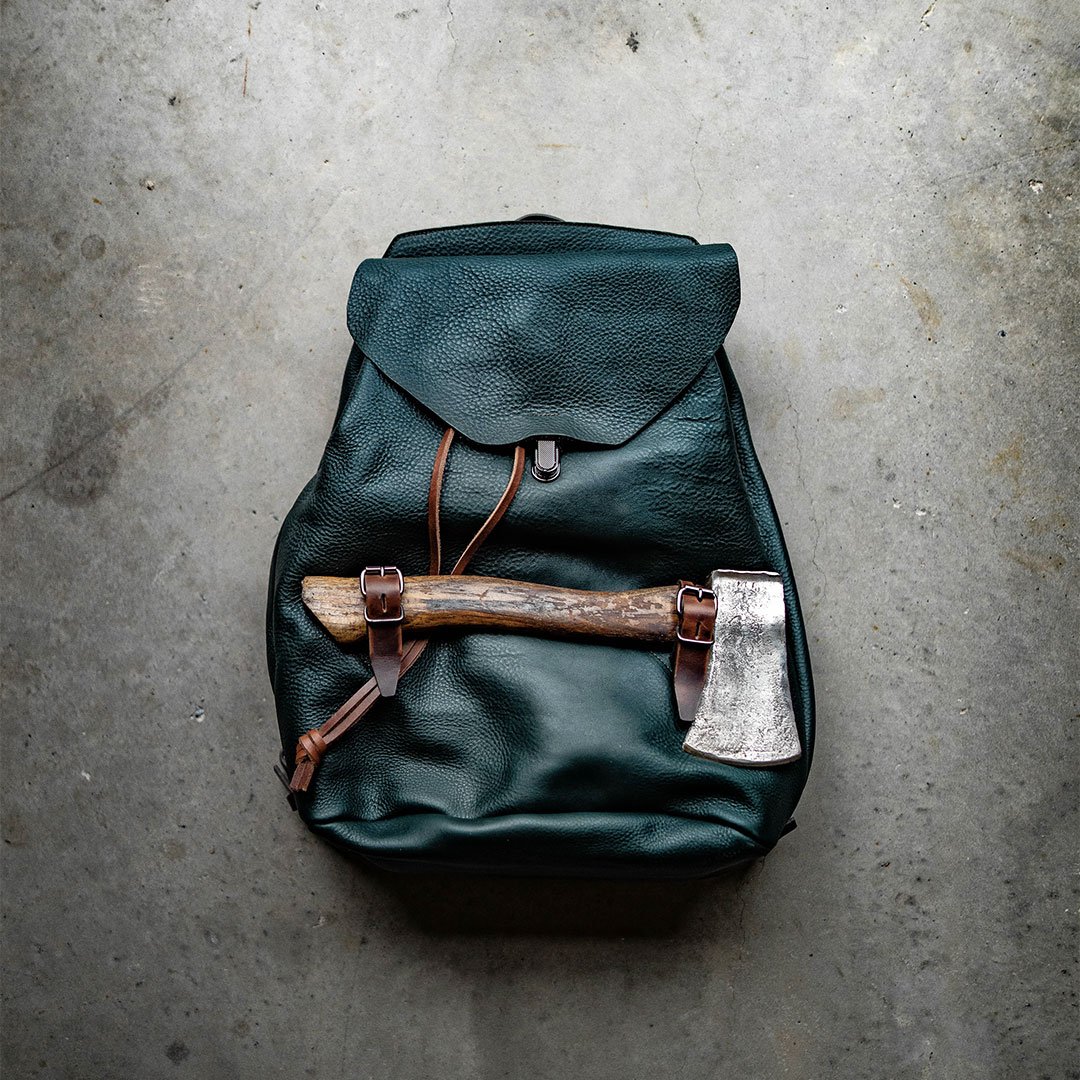 An axe hangs from a leather backpack