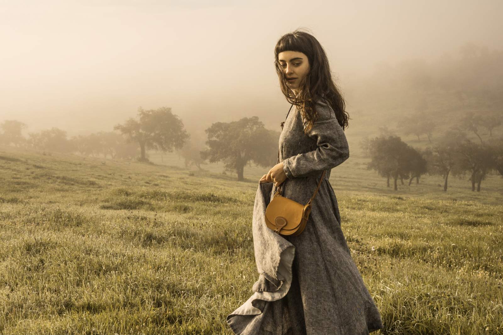 Un femme porte une gibeciere en cuir en bandoulière dans un champ 